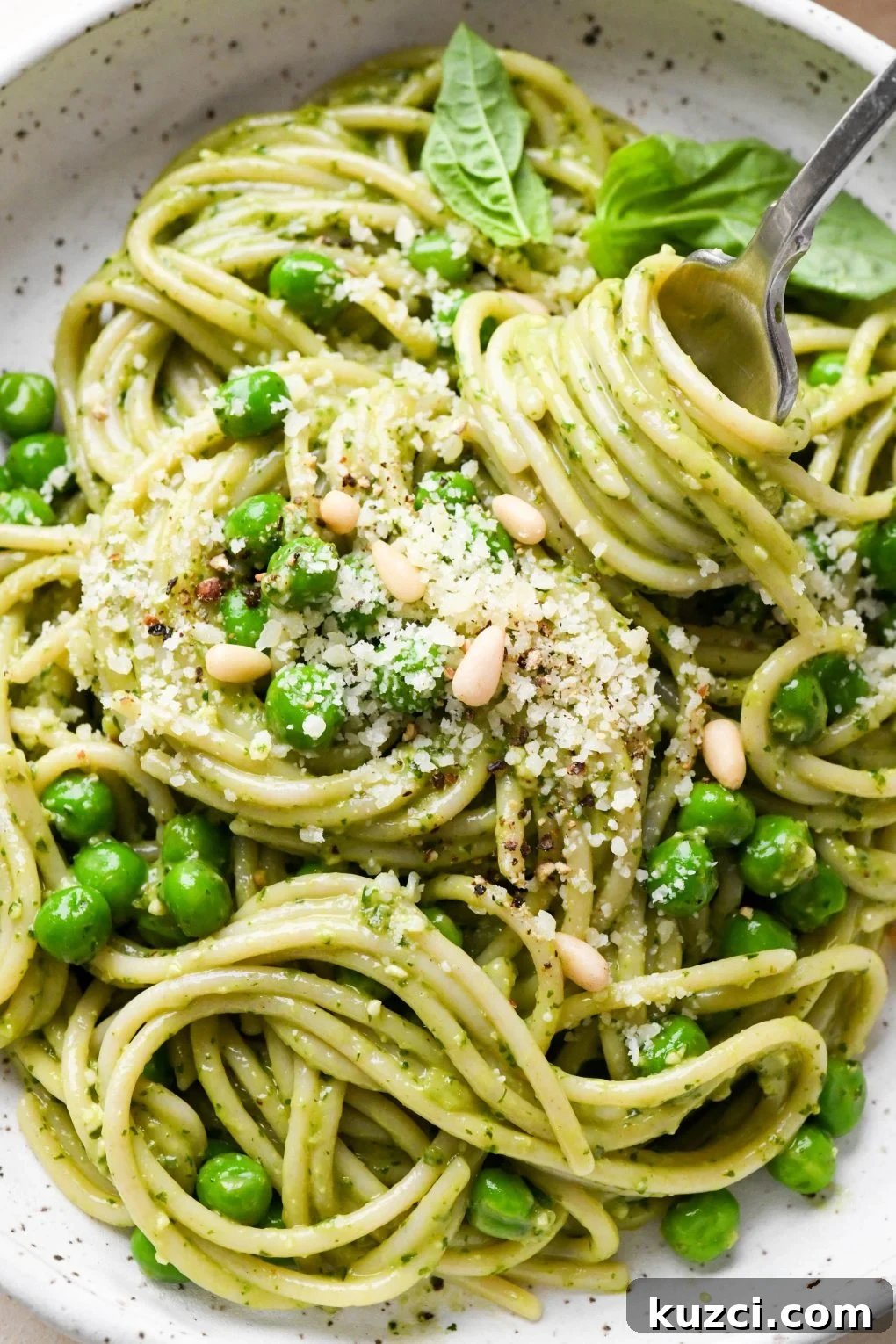 Homemade Basil Pesto - Vegan-Friendly Recipe 10 Pesto pasta made with spaghetti in a speckled ceramic bowl with a fork twirling a bite, topped with pine nuts and grated parmesan.
