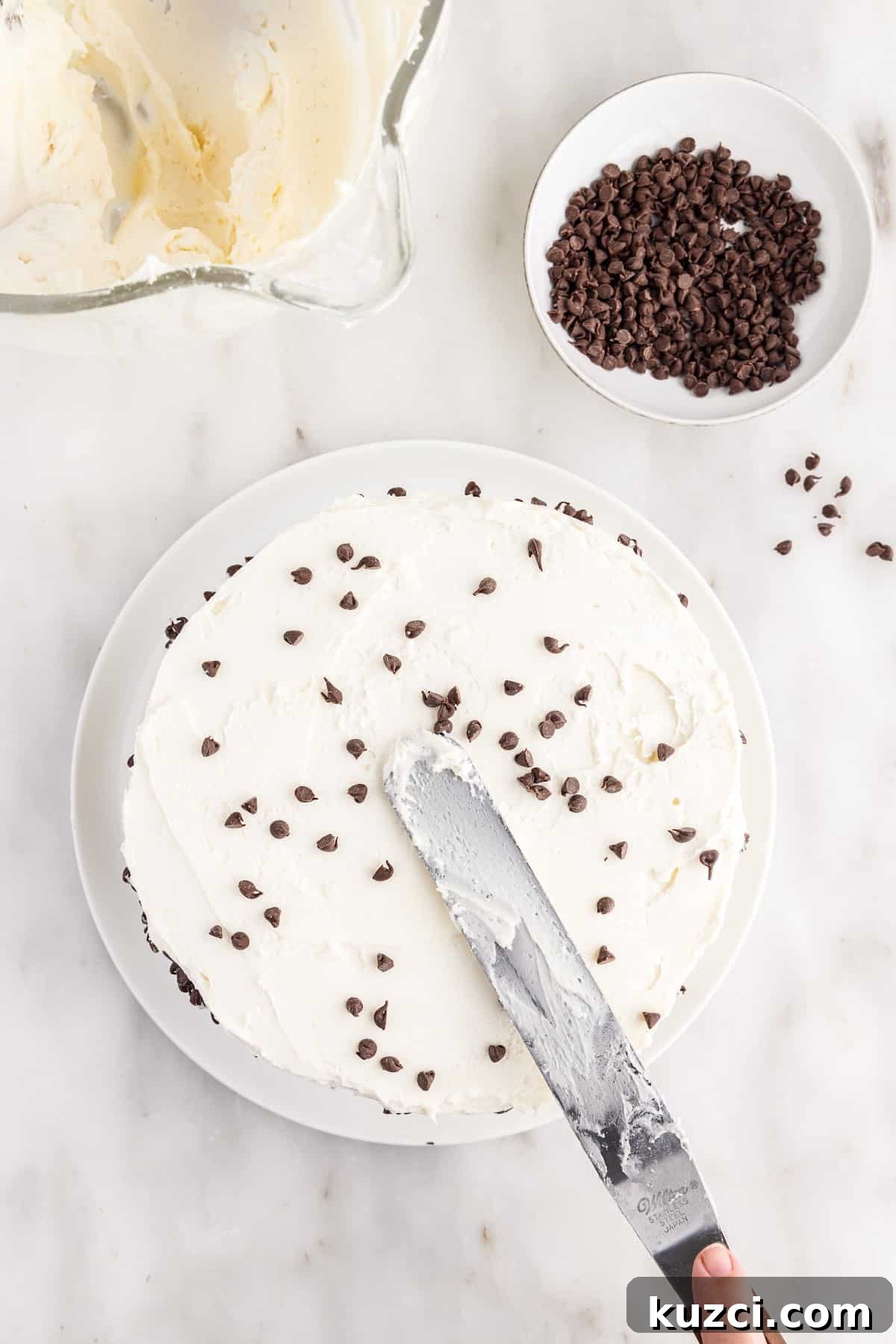 Moist Chocolate Chip Cake Recipe 15 Sprinkling the mini chocolate chips on the top of the fully frosted cake, with other ingredients in the background.