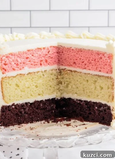 Neapolitan Cake frosted with white frosting, sliced open showing the layers.