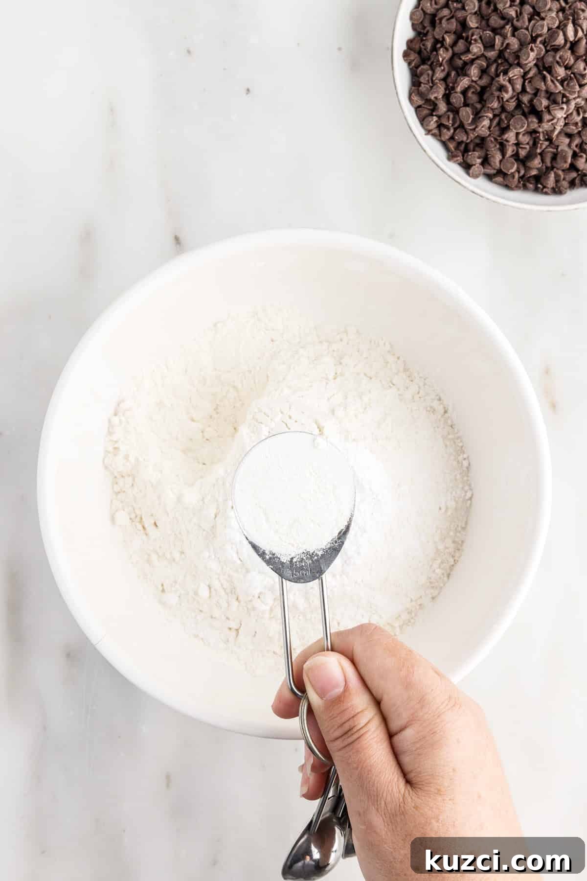 Moist Chocolate Chip Cake Recipe 4 Mixing the dry ingredients together in a bowl, with other ingredients in the background.