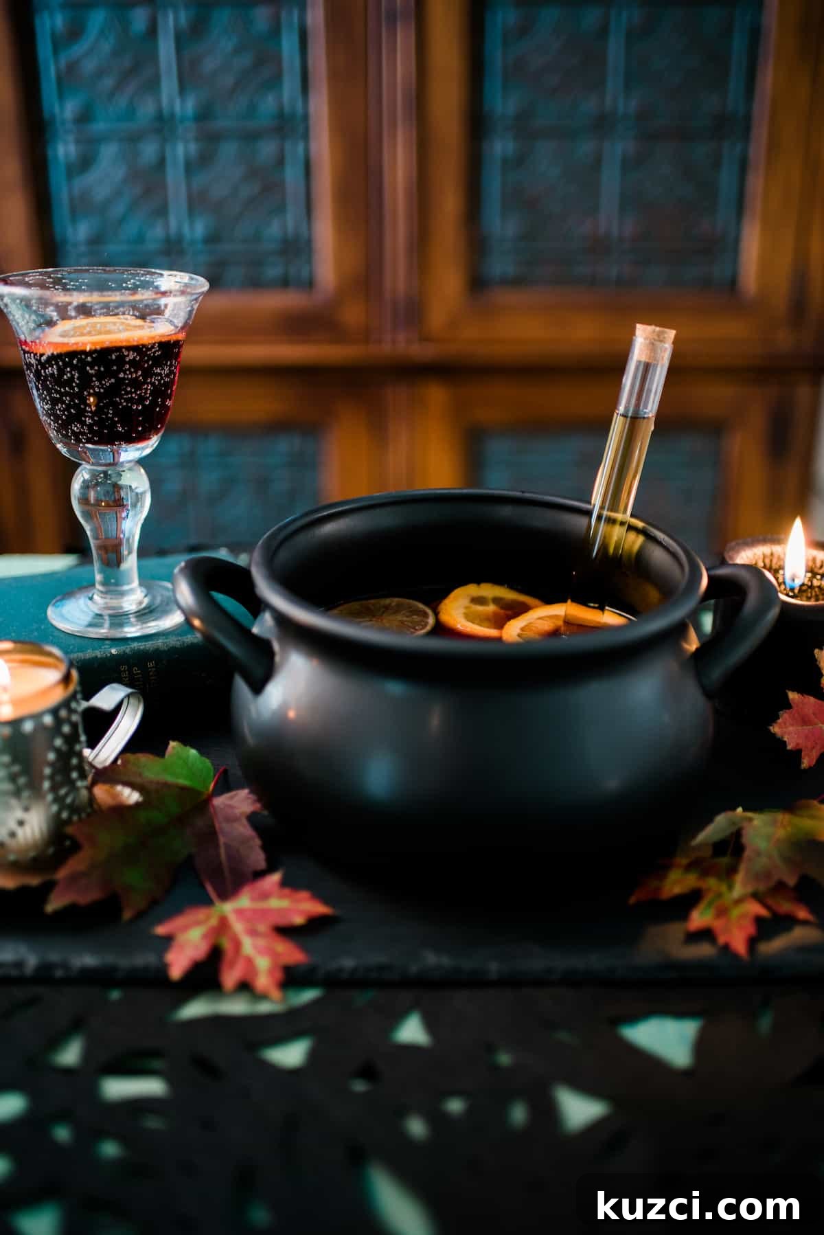Witches' Brew Sangria: Spooky Halloween Cocktail 6 Halloween tablescape with a black witch’s cauldron filled with sangria, a liquor-filled test tube, fall leaves, and glowing candles.