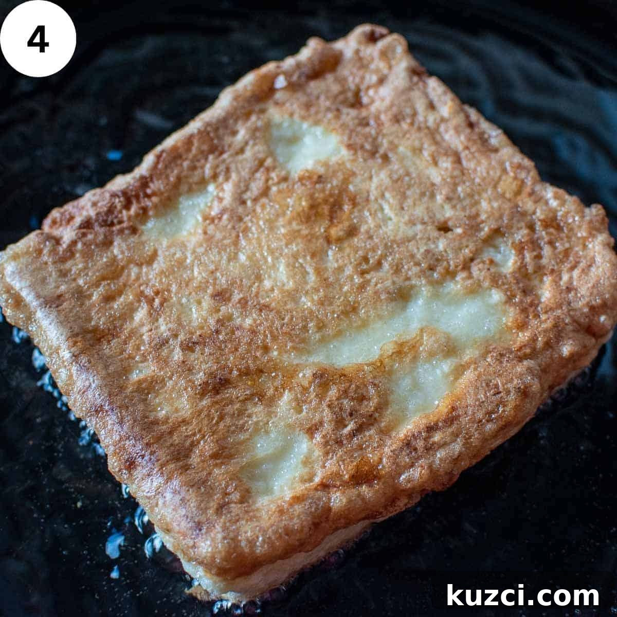 Sandwich of eggy bread frying in oil in a skillet.