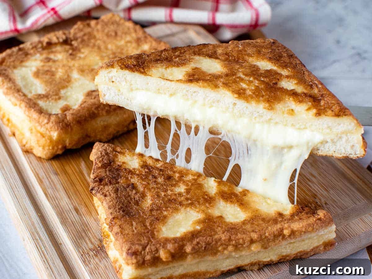 Fried sandwich cut in half and showing cheese pull with second sandwich in background.