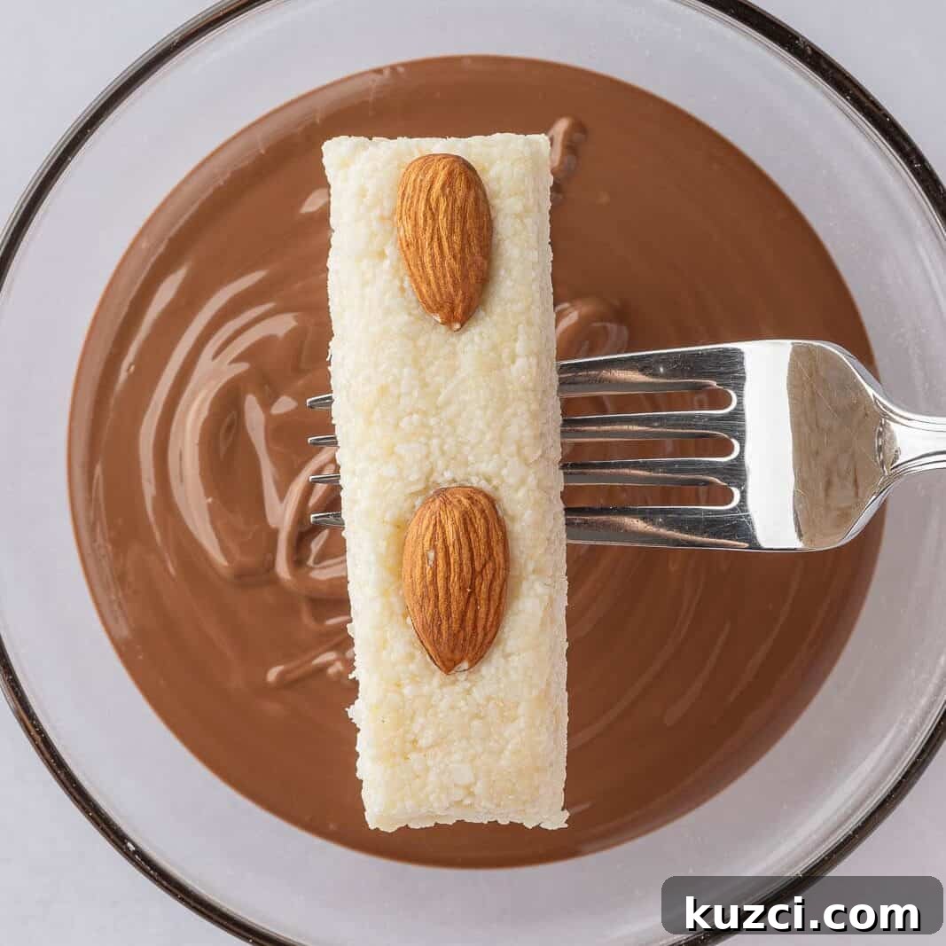 No-Bake Coconut Chocolate Bar Recipe 7 Candy bar filling is dipped into melted chocolate with a fork.