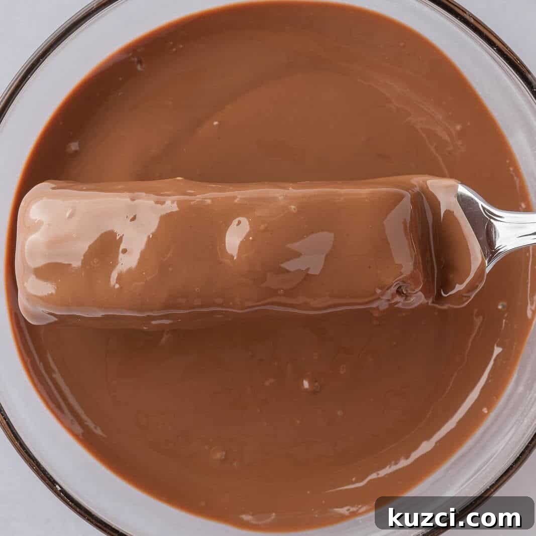 No-Bake Coconut Chocolate Bar Recipe 8 A fork dips a candy bar into a bowl of melted chocolate.
