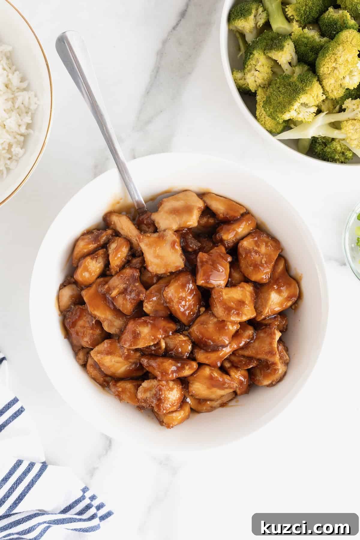 Chunks of chicken in a brown sauce in a white serving bowl on a white marble counter.