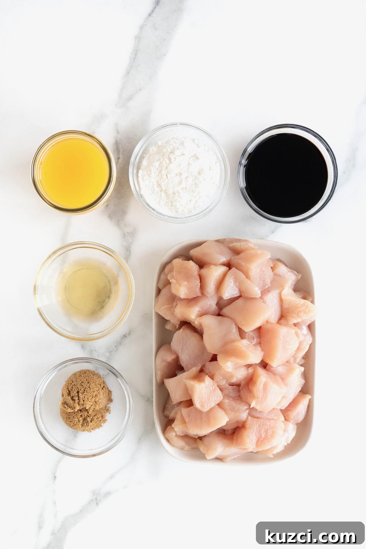 Ingredients to make baked orange chicken in small glass dishes on a white marble counter.