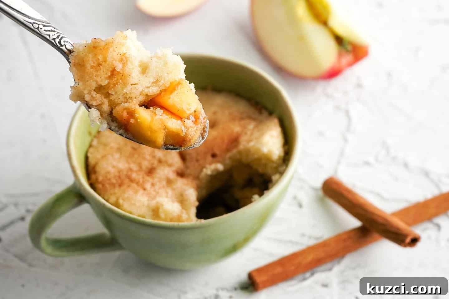 Microwave Apple Cinnamon Mug Cake Recipe 2 Spoon with apples and cake being held over cake in a green mug