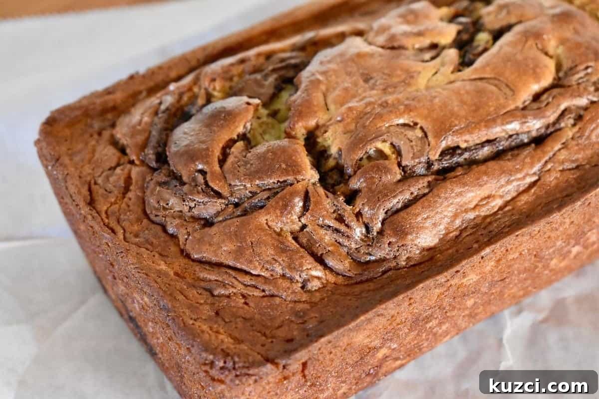 Loaf of Nutella Swirl Banana Bread on a piece of parchment paper on a countertop.