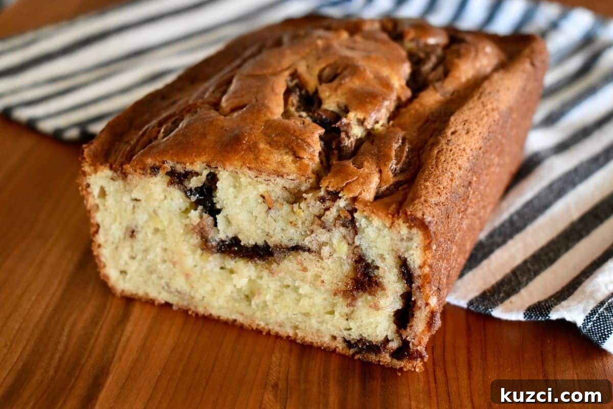 Nutella Swirl Banana Bread on a wood cutting board with a striped towel under it.