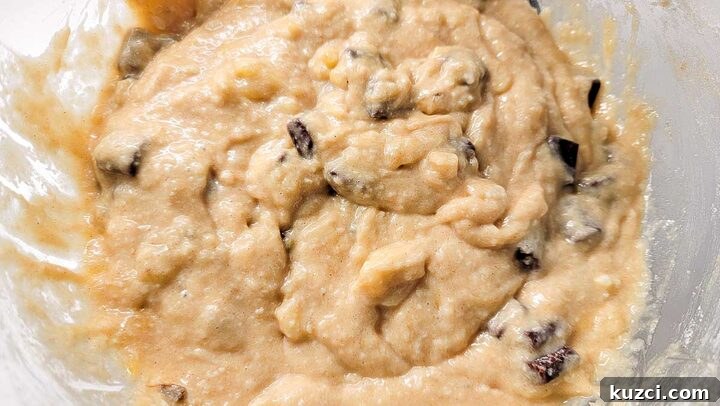 mashed banana, butter, sugar, eggs, vanilla, flour, baking soda, salt, and chocolate chunks mixed in a bowl.