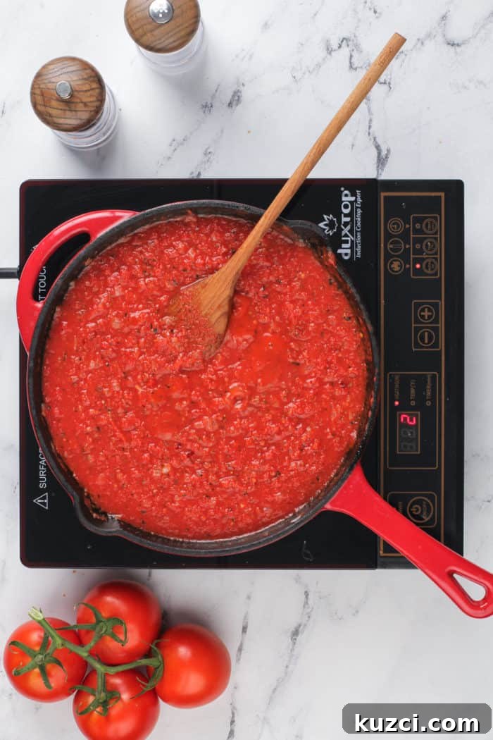 15-Minute Homemade Marinara Sauce for Pasta 7 Quick tomato sauce in a skillet, set on a wood and marble board and surrounded by tomatoes, garlic, and basil.