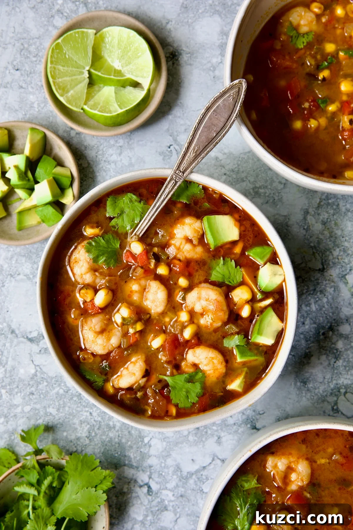 Creamy Shrimp and Corn Soup Recipe 12 Shrimp and Corn Soup in white bowl with soup spoon garnished with cilantro and lime wedge.
