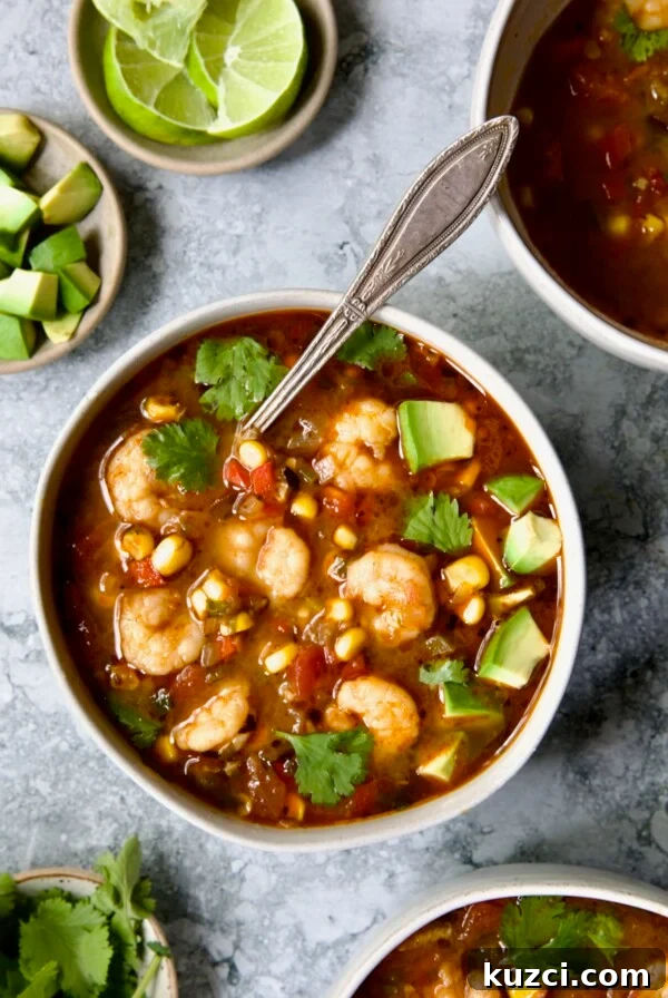 Creamy Shrimp and Corn Soup Recipe 14 Shrimp and Corn Soup in white bowl with soup spoon garnished with cilantro and lime wedge.