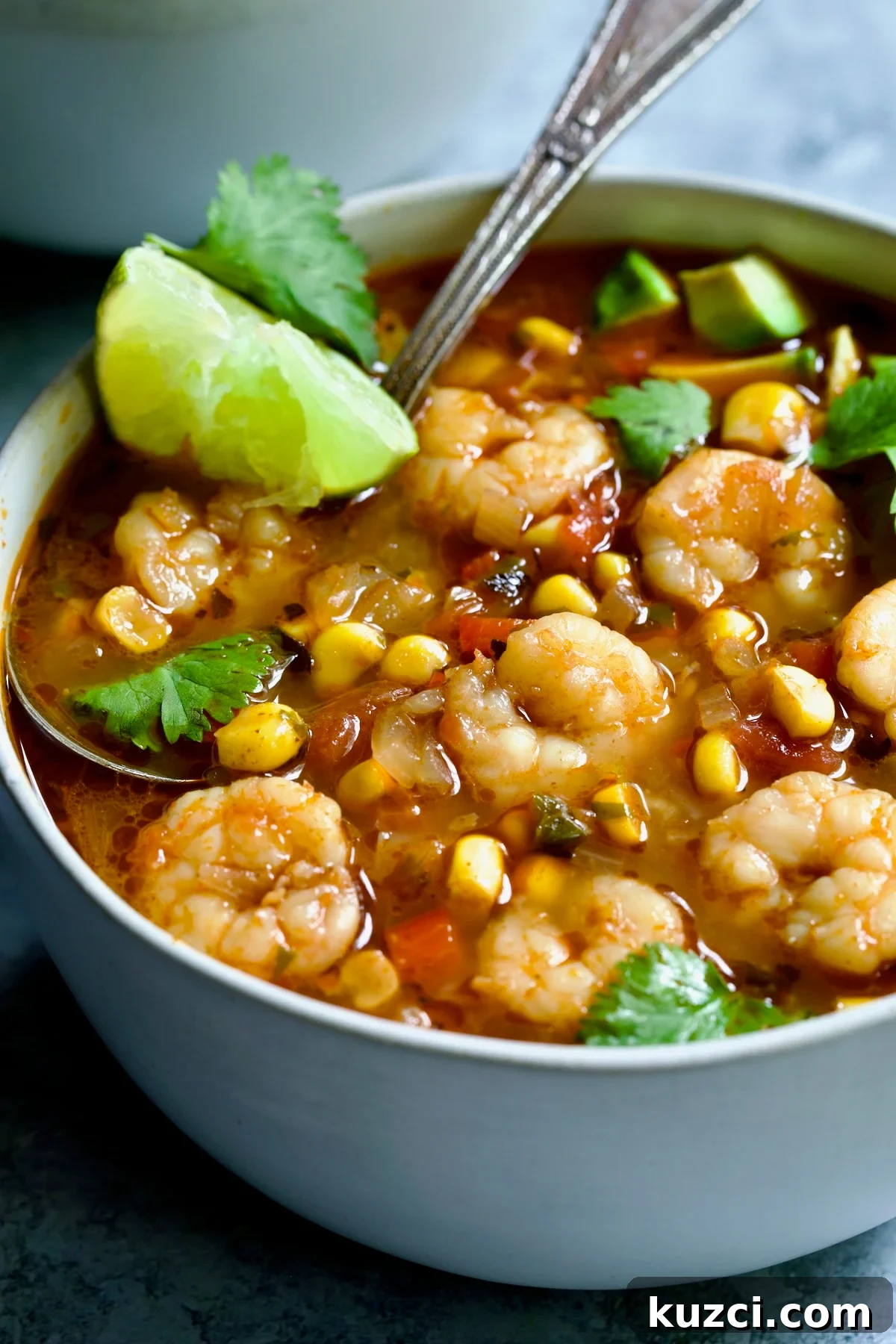 Creamy Shrimp and Corn Soup Recipe 3 Shrimp and Corn Soup in white bowl with soup spoon garnished with cilantro and lime wedge.