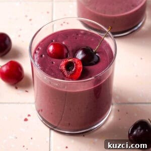 A cherry smoothie served in a small glass sitting on a tile counter.