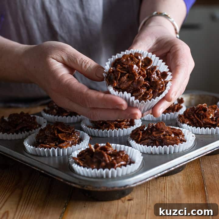 No-Bake Chocolate Cornflake Cakes Recipe 3 womans hands holding a chocolate cornflake cake over a full tray of cakes