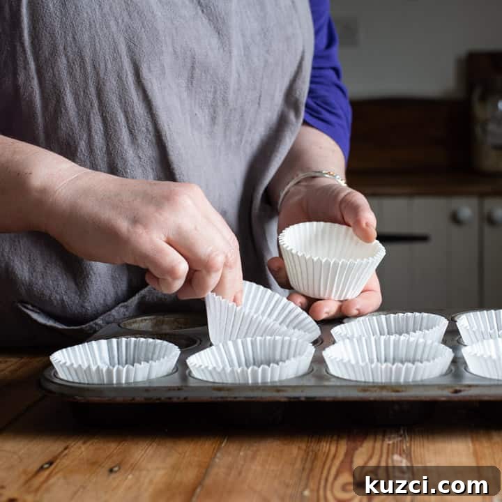 No-Bake Chocolate Cornflake Cakes Recipe 8 womans hands placing white cupcake cases into a silver cupcake baking tin