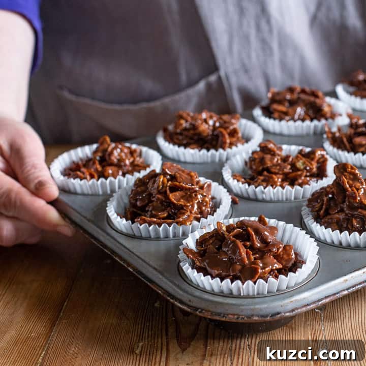 No-Bake Chocolate Cornflake Cakes Recipe 10 womans hands holding a silver metal tray of white paper cases filled with chocolate covered cornflakes