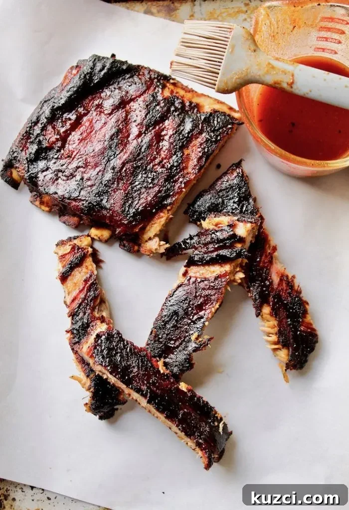 Ribs off the grill, cut into sections with basting sauce in background.