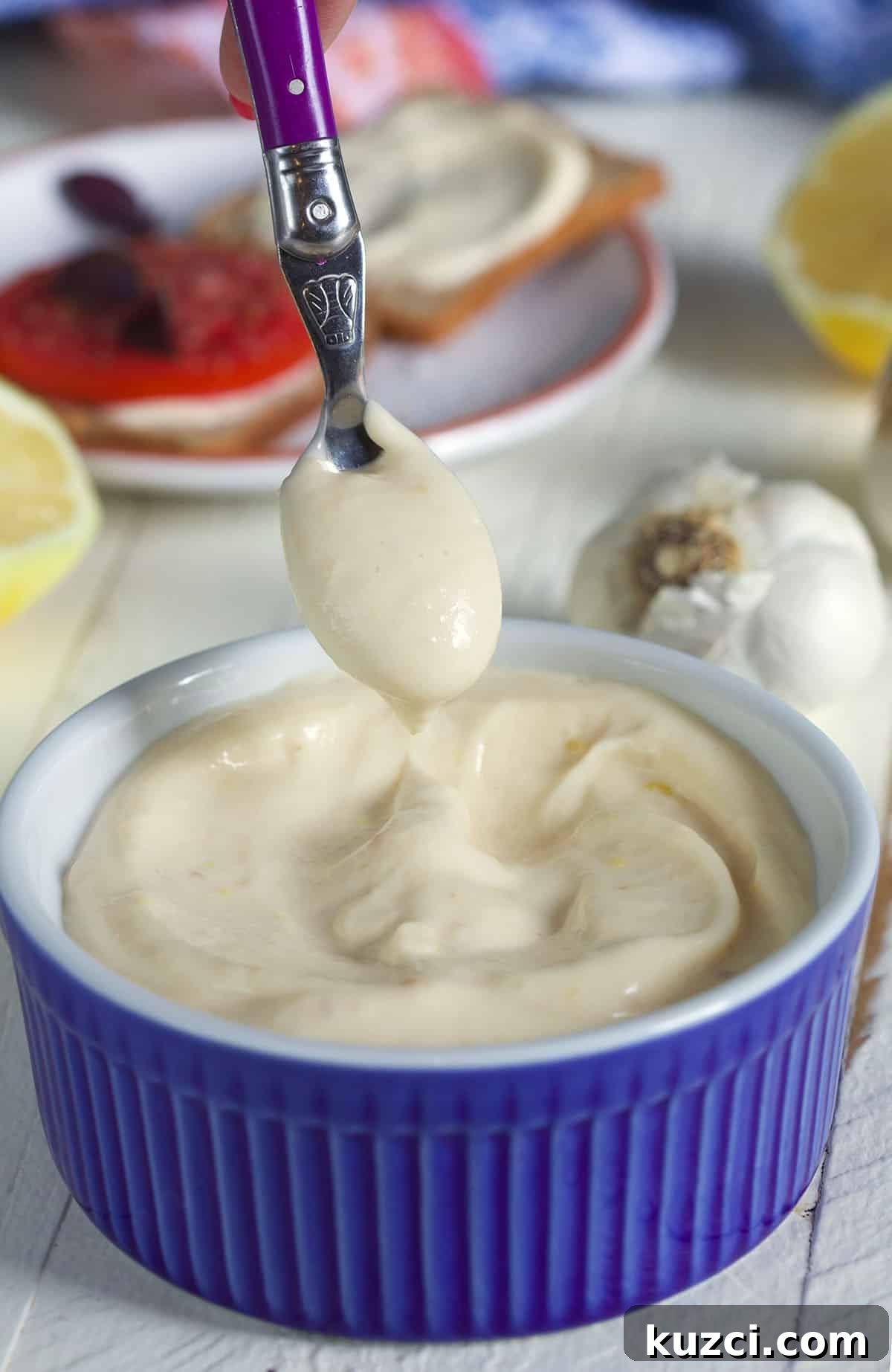 How to Make Roasted Garlic Aioli 2 Garlic Aioli in a blue bowl with a scoop on a purple spoon.