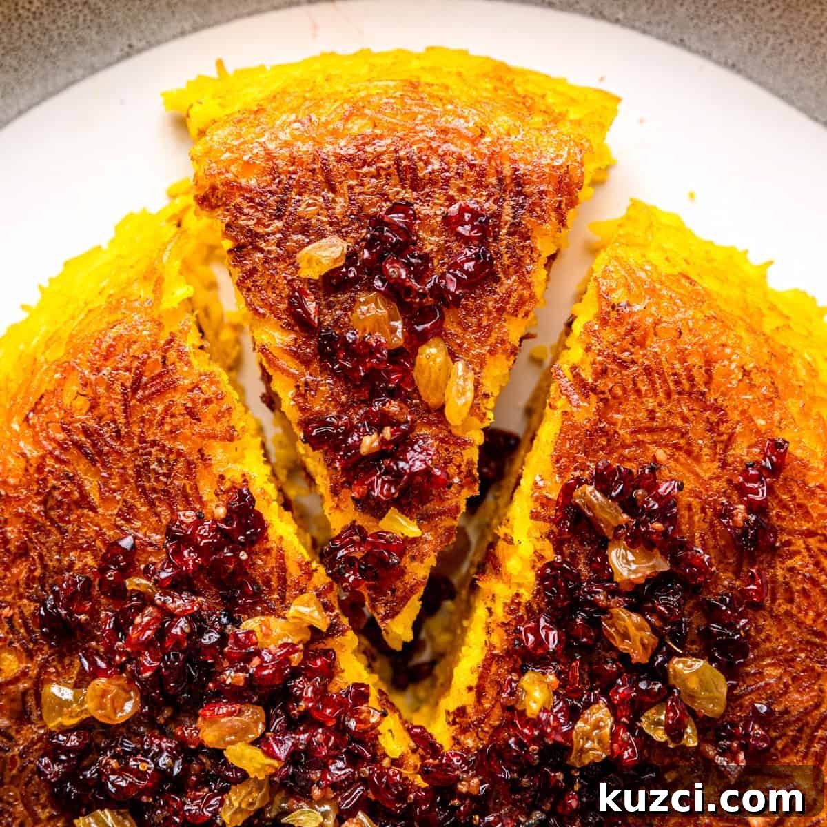 overhead closeup: wedge of baked tachin topped with dried barberries and golden raisins