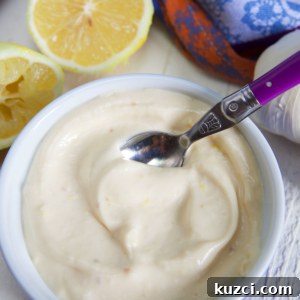 How to Make Roasted Garlic Aioli 6 garlic aioli in a blue and white ramekin with a purple handled spoon in it and a sliced lemon on the side.