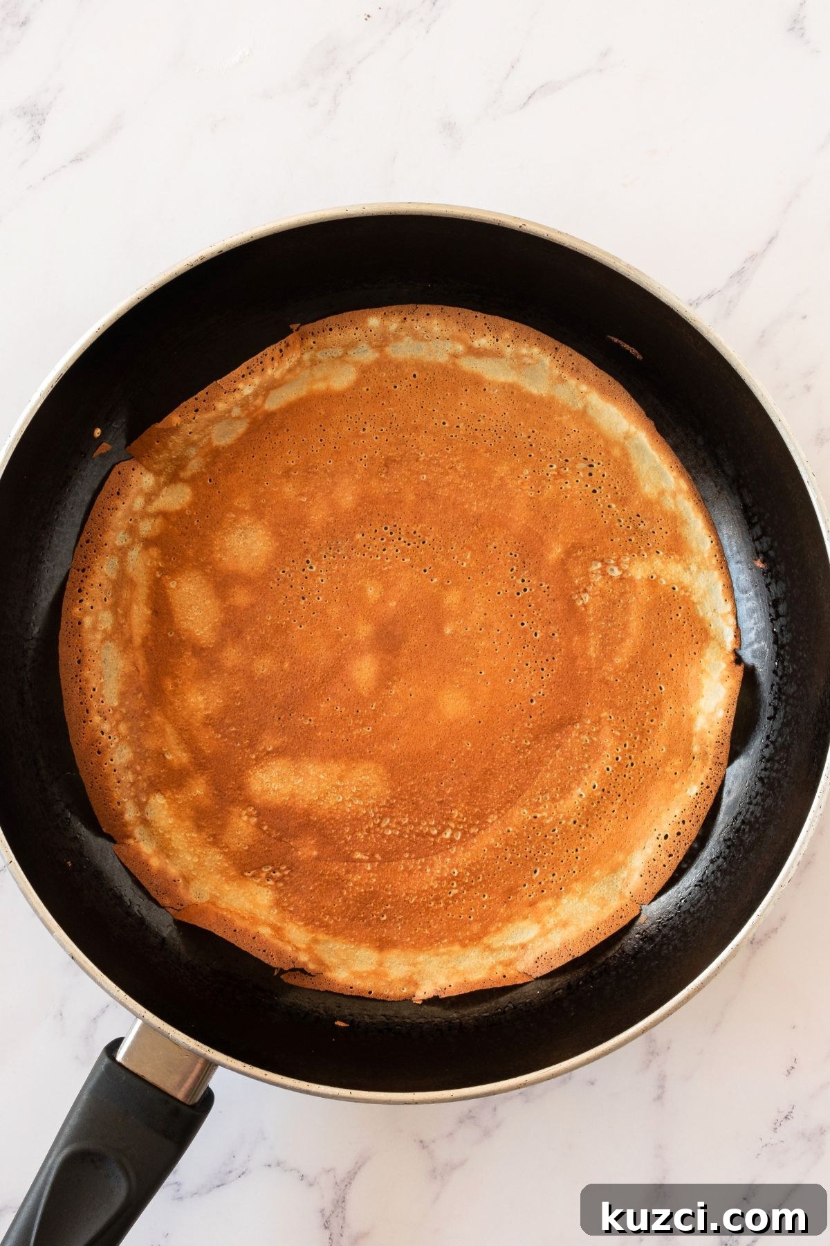 Classic French Crepe Cake (Mille Crepes) Recipe 4 Very thin crepes being made in a black skillet, cooked until golden brown.