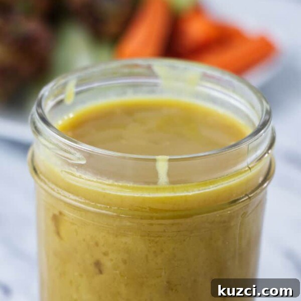 Avocado Lime Crema Recipe 12 brownish yellow honey mustard sauce in mason jar with chicken wings and carrots and celery on a white plate in the background