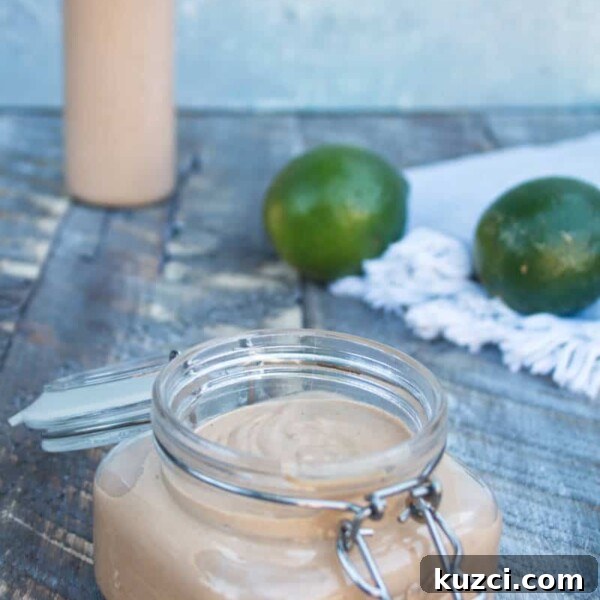 Avocado Lime Crema Recipe 14 chipotle lime crema in a mason jar sitting on a wood plank surface with two whole limes in the background