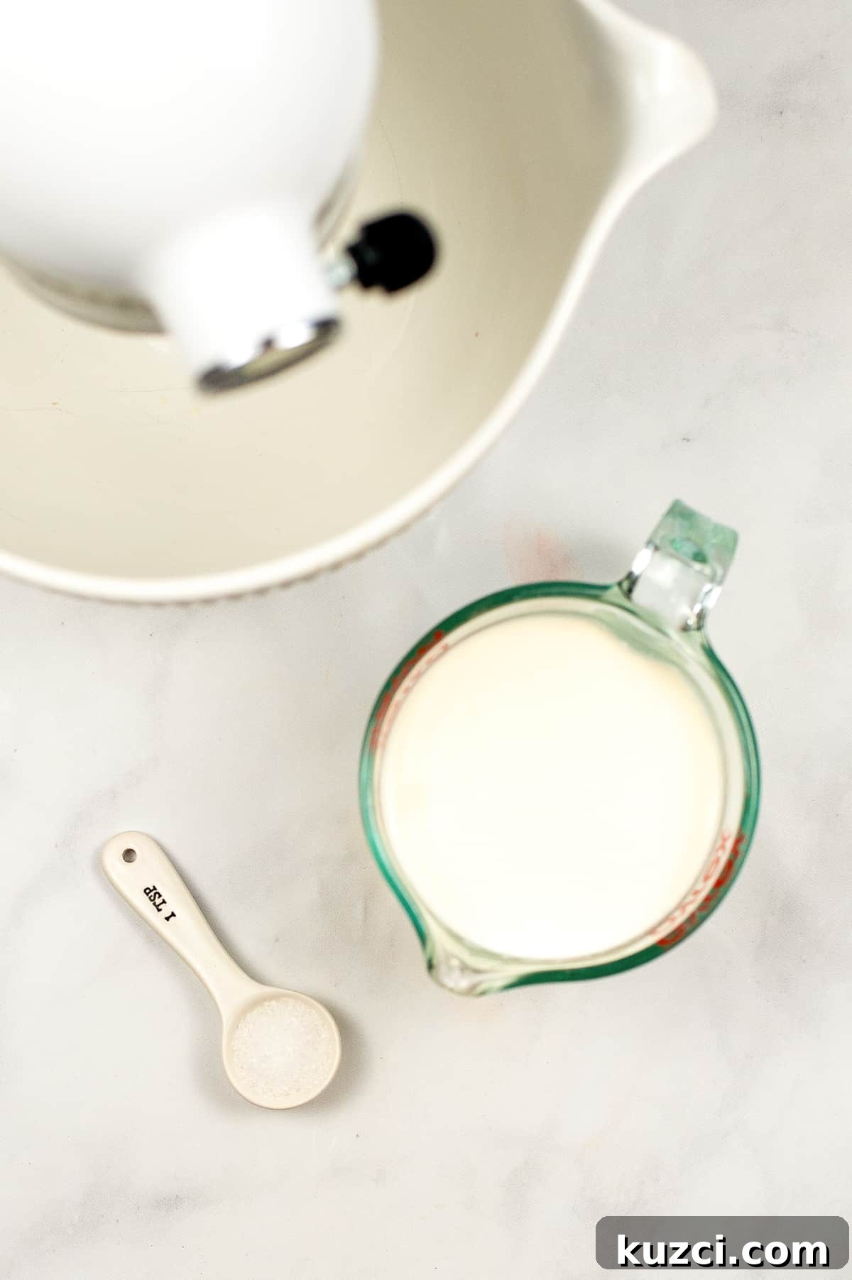 Stand mixer, measuring cup filled with cream, and teaspoon of salt