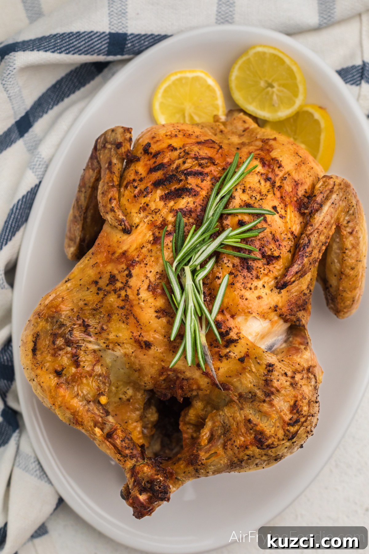 Crispy Whole Chicken in the Air Fryer 8 Air fried whole chicken on a serving plate with rosemary sprigs on the top and served with lemon slices.
