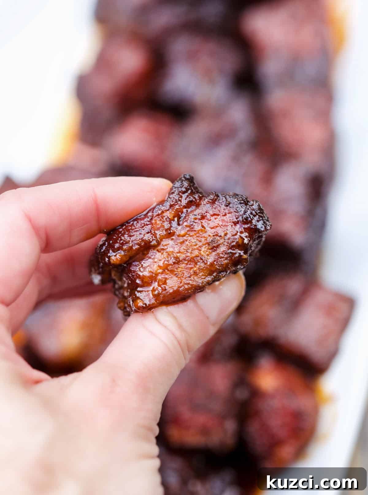 Smoked Pork Belly Burnt Ends: How to Make Sticky, Crispy Bites 8 A hand holding a single smoked pork belly burnt end bite