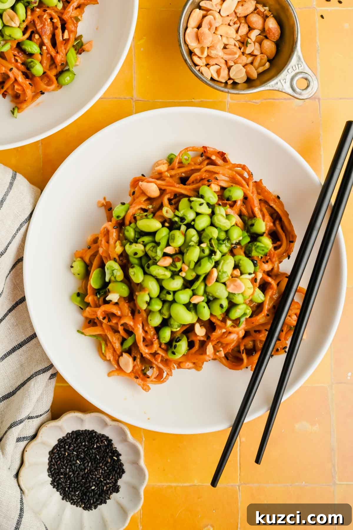 Spicy Peanut Noodles with Chili Garlic Sauce 2 spicy peanut noodles on white plate topped with herby edamame mixture.