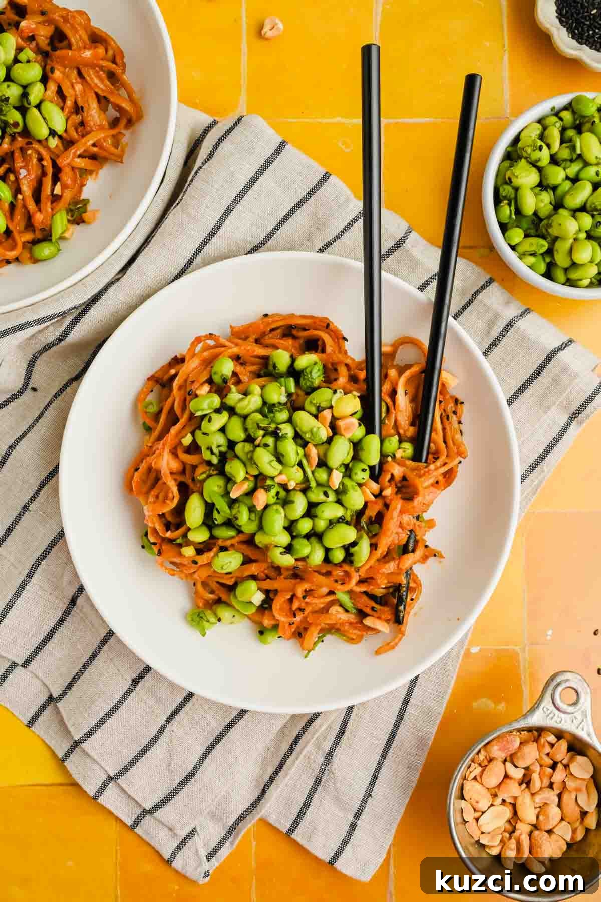 Spicy Peanut Noodles with Chili Garlic Sauce 11 spicy peanut noodles on white plate topped with herby edamame mixture.