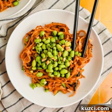 Spicy Peanut Noodles with Chili Garlic Sauce 12 spicy peanut noodles on white plate topped with herby edamame mixture.