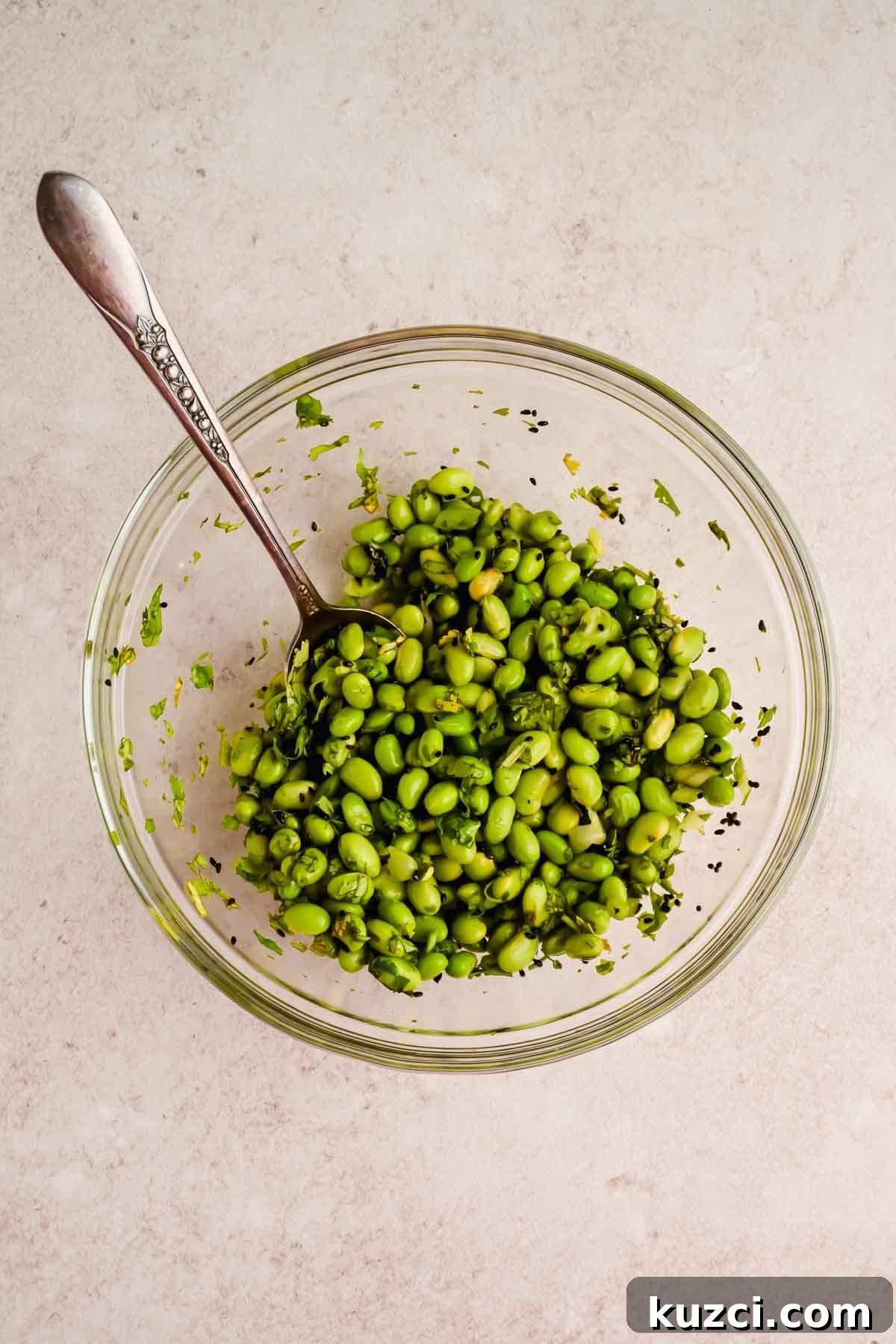 Spicy Peanut Noodles with Chili Garlic Sauce 8 edamame and herbs mixed together in glass mixing bowl.