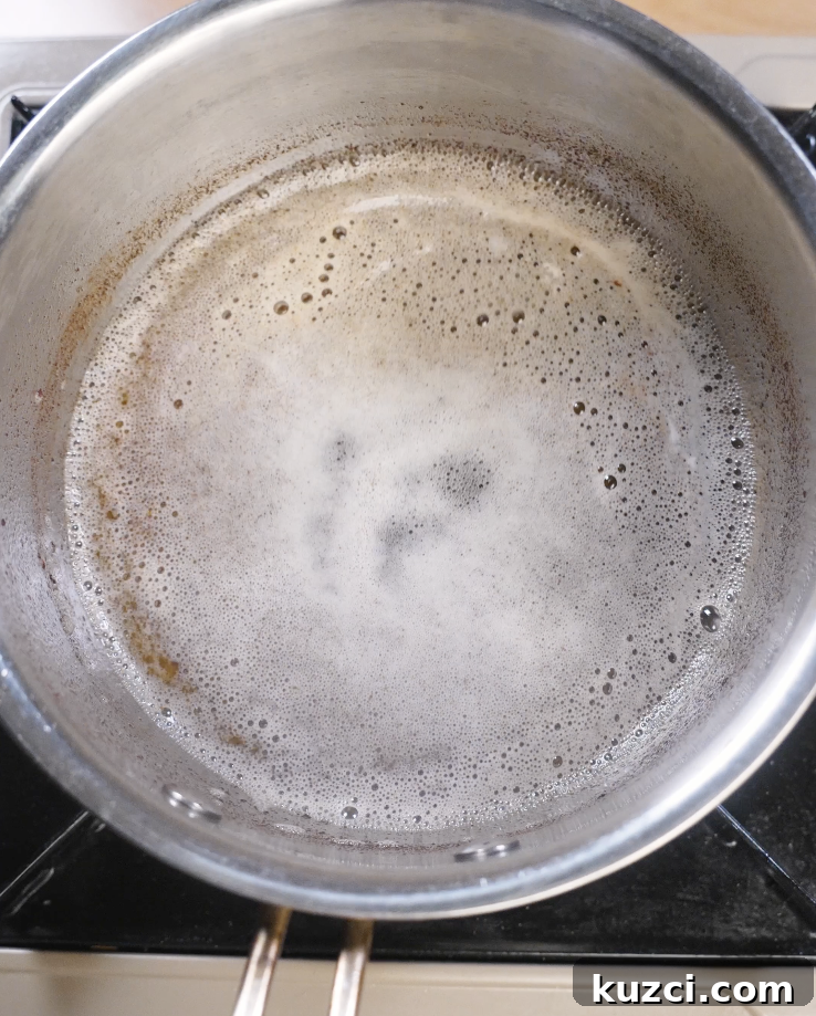 Unsalted butter melting and foaming in a saucepan over medium heat as the milk solids begin to brown, creating nutty brown butter for chocolate chip cookies.