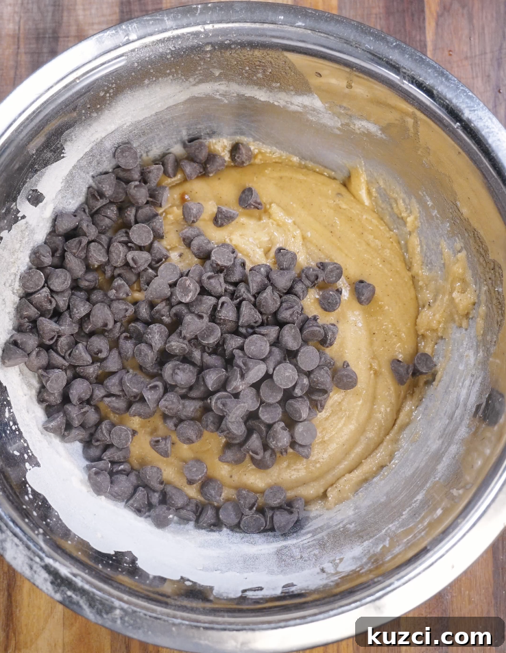 Dark chocolate chips scattered over brown butter cookie dough before folding in for even chocolate distribution.