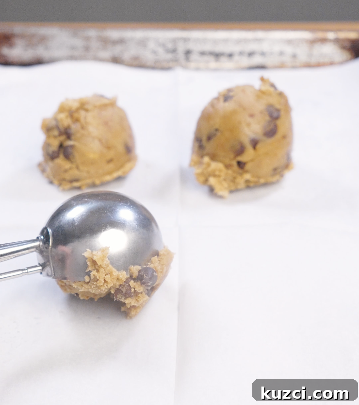 Large scoops of brown butter chocolate chip cookie dough portioned onto parchment paper using a cookie scoop.