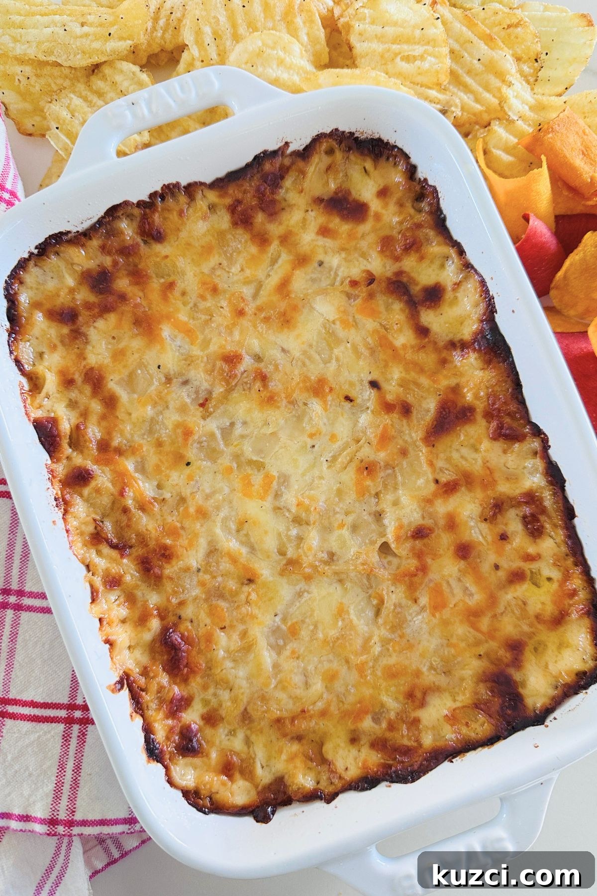 Creamy Baked Onion Dip Recipe with Caramelized Onions 2 Hot onion dip in a large white baking dish surrounded by potato chips.