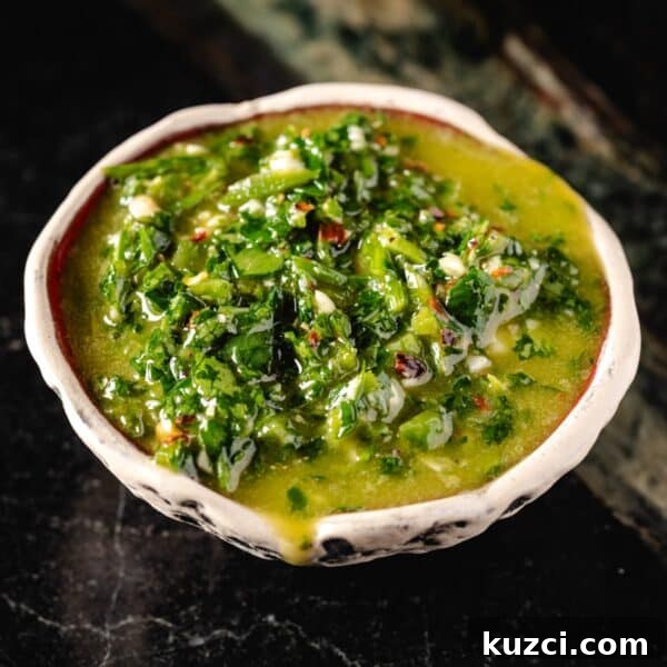 A white bowl filled with jalapeño chimichurri sauce on a marble surface.