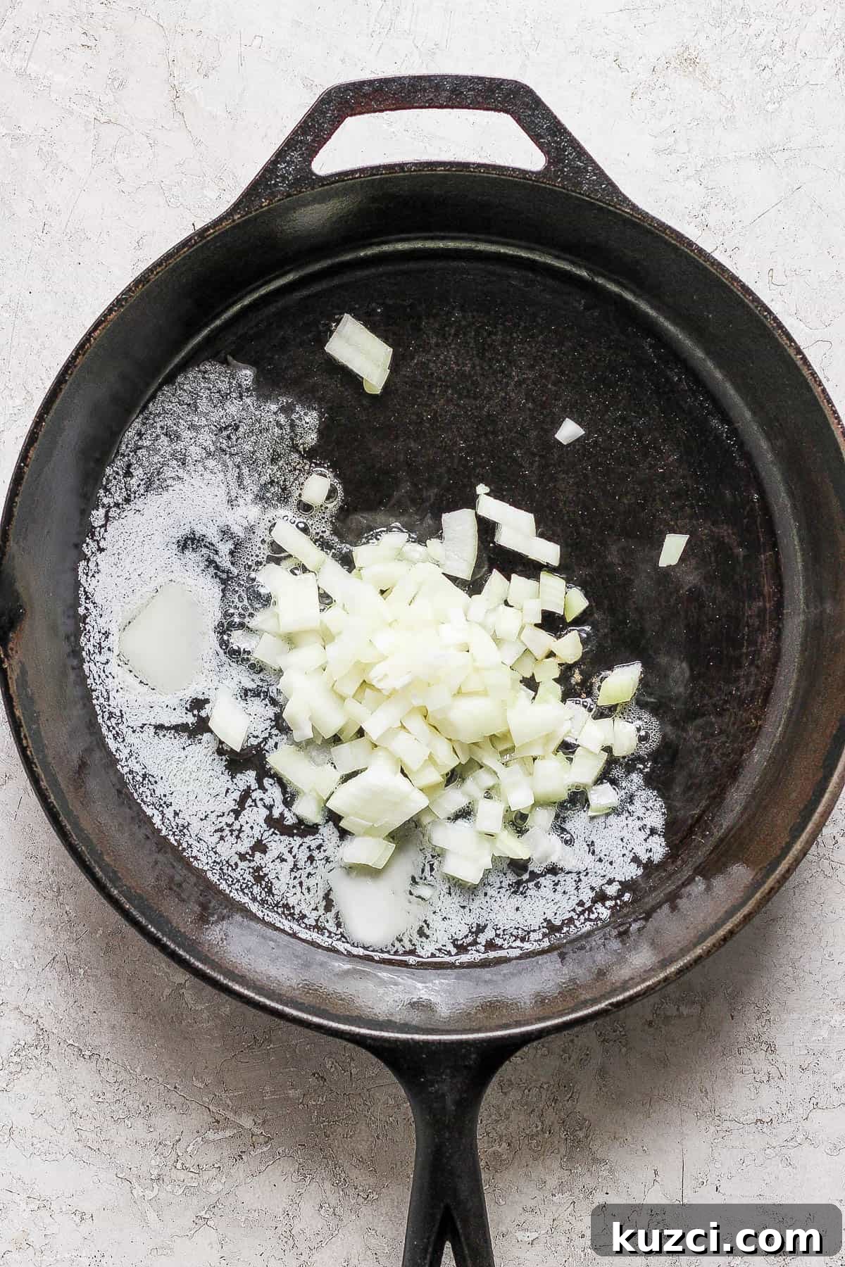 Butter melting in a cast iron skillet with chopped onions added.