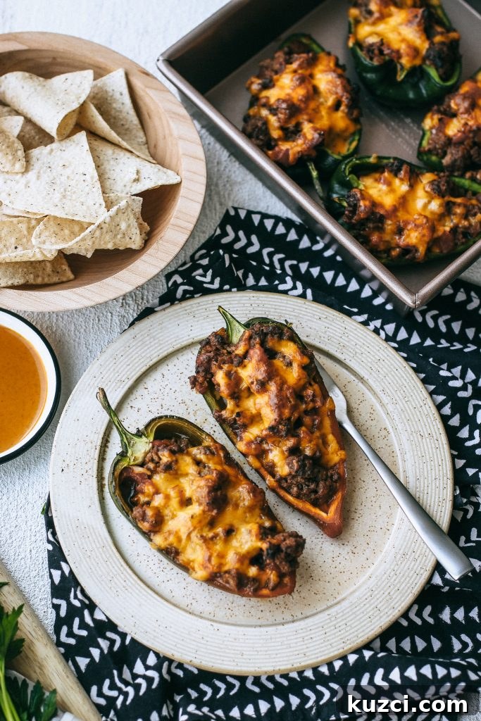Spicy Low-Carb Stuffed Poblano Peppers Recipe 2 cheesy stuffed peppers on a plate with peppers in a baking dish and a bowl of tortilla chips