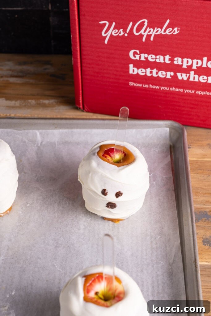 5-Ingredient Halloween Caramel Apples Recipe 10 Dark chocolate used to make eyes and a mouth on a caramel and white chocolate covered apple.