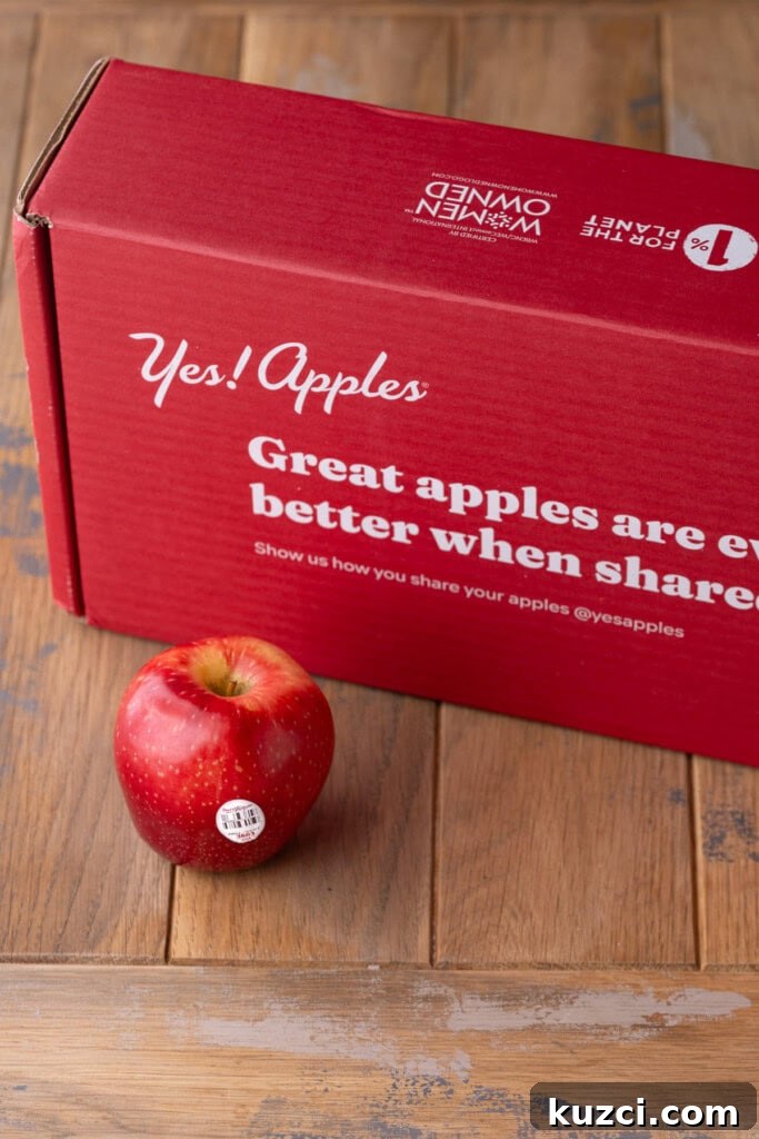 5-Ingredient Halloween Caramel Apples Recipe 4 Yes Apples box on a wooden surface with one Sweet Tango Apple out in front.