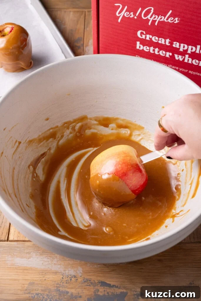 5-Ingredient Halloween Caramel Apples Recipe 8 Dunking a red apple in melted caramel to coat.