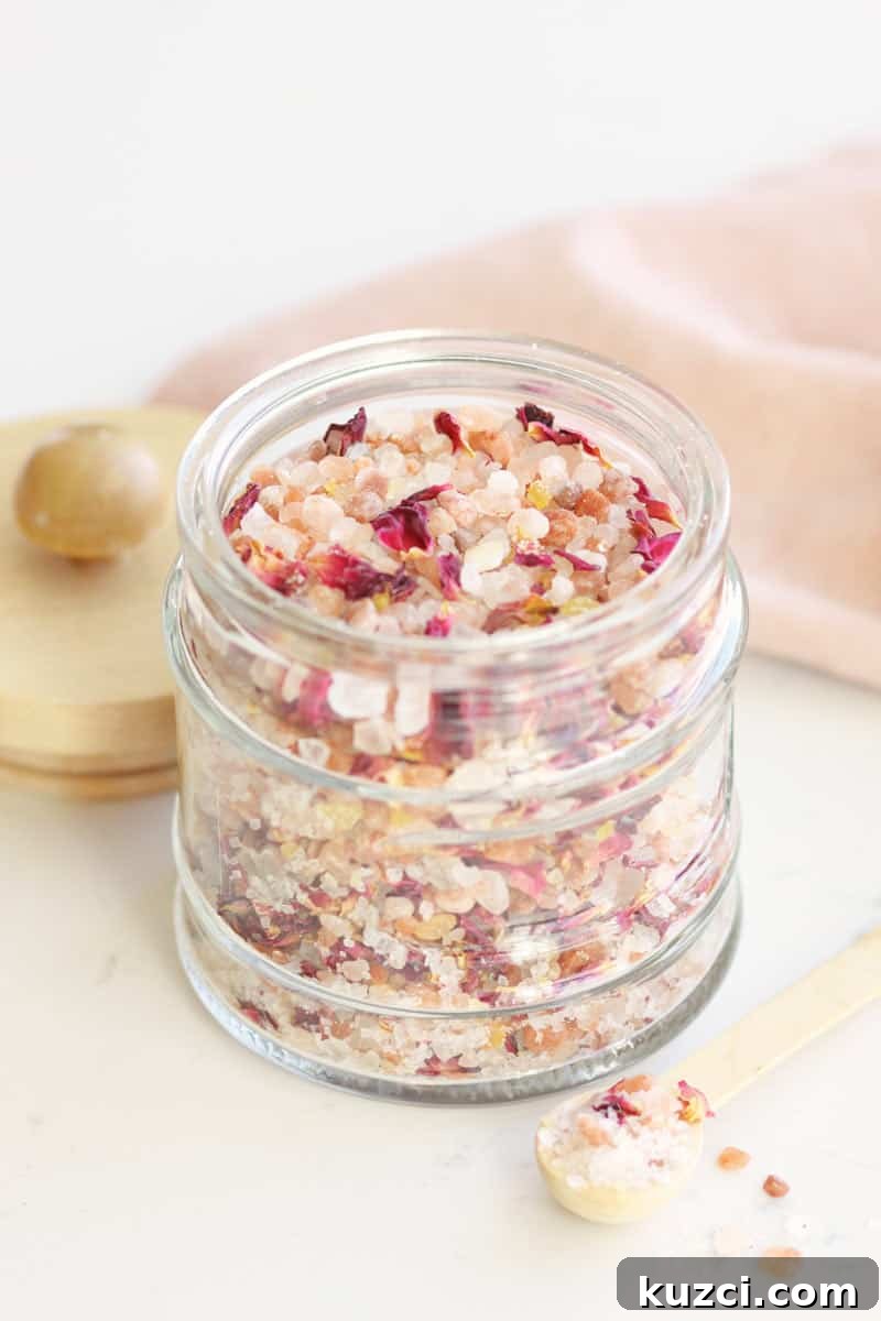 Homemade Rose Petal Bath Salts Recipe 2 a small glass jar with a wooden lid and small wooden spoon full of rose bath salts with rose petals in it.