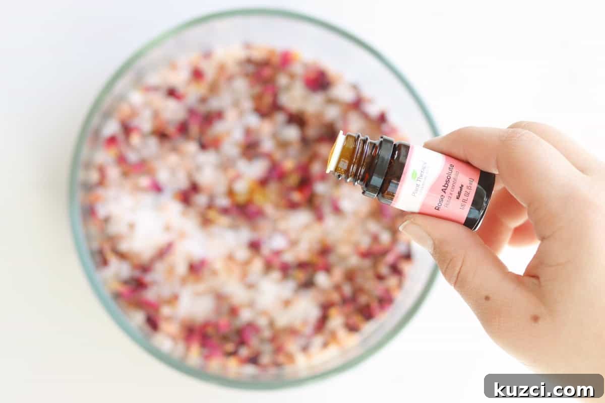 Homemade Rose Petal Bath Salts Recipe 3 drops of rose essential oil being added to a bowl of sea salt, Himalayan pink salt and rose petals to make bath salts