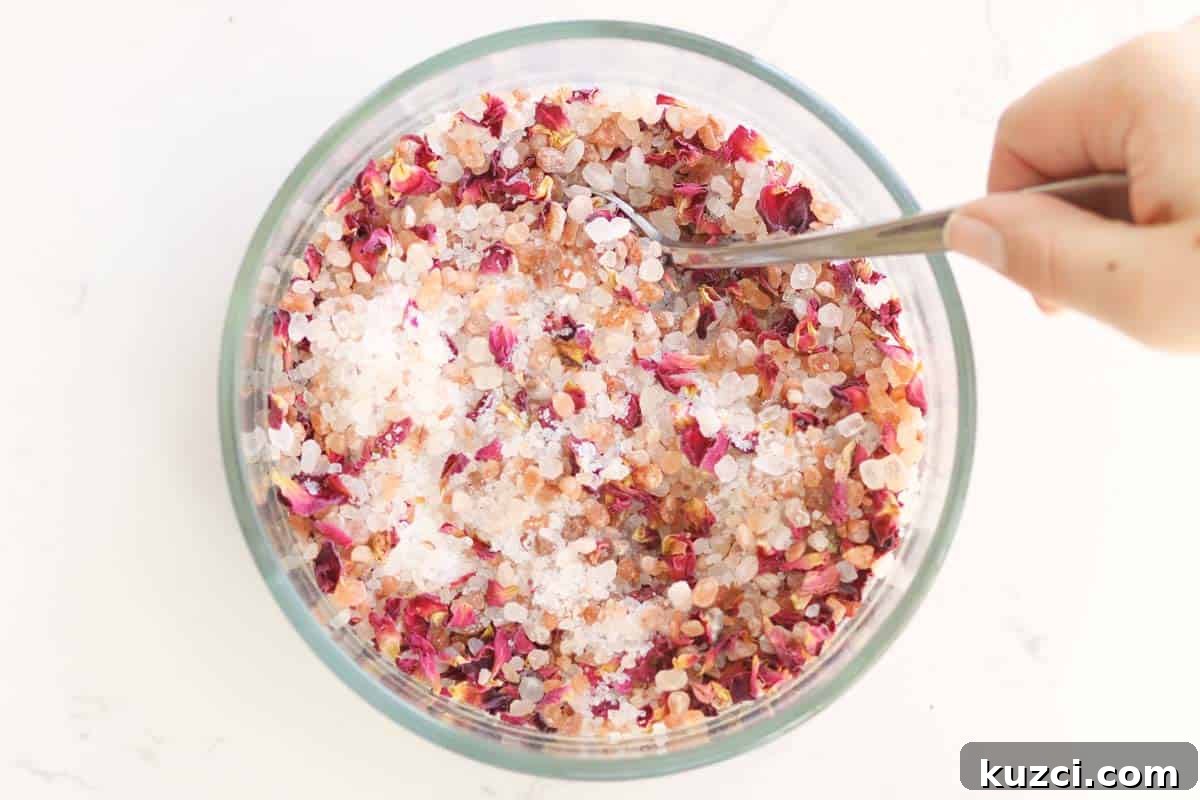 Homemade Rose Petal Bath Salts Recipe 6 a bowl of sea salt, Himalayan pink salt and rose petals being stirred with a spoon.